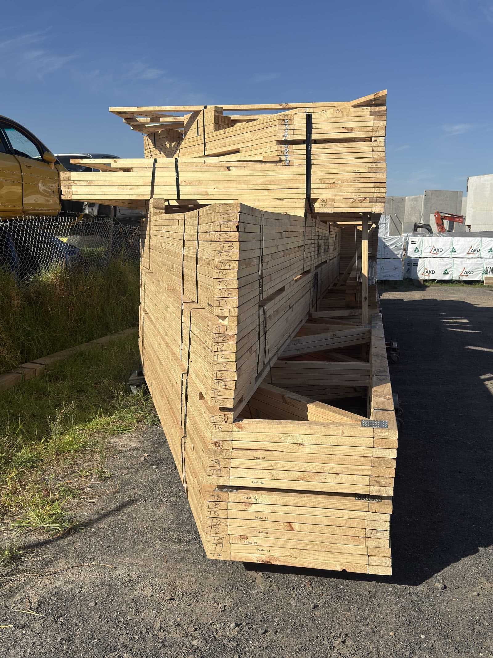 Assembled wall frame with roof truss components visible, marked with hand-written notes, standing in yard near truck.